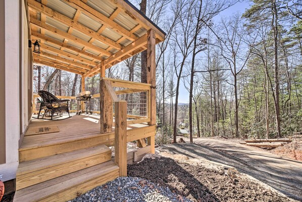 A wooden deck with outdoor furniture, surrounded by a forest. - Modern Cabin w/ Fire Pit < 3 Mi to Trails! (Pisgah Forest)