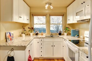 A kitchen with white cabinets, a granite countertop, a built-in oven, and a window with a view of trees.