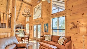Una cabaña de madera espaciosa con comedor, sala de estar con sofá y banca, y ventanas amplias con vistas al exterior.