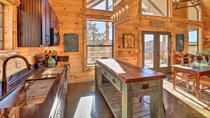 Un interior rústico de madera con una zona de cocina que incluye una isla grande, armarios de madera y una mesa de comedor con sillas.