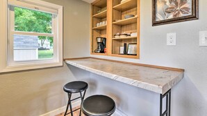 A kitchen with a marble countertop, two black stools, wooden shelves, and a framed floral artwork on the wall. - Centrally Located Mount Pleasant Retreat! (Mount Pleasant)