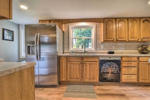 Cocina moderna con armarios de madera, refrigerador de acero inoxidable, lavavajillas y ventana con vista a árboles.