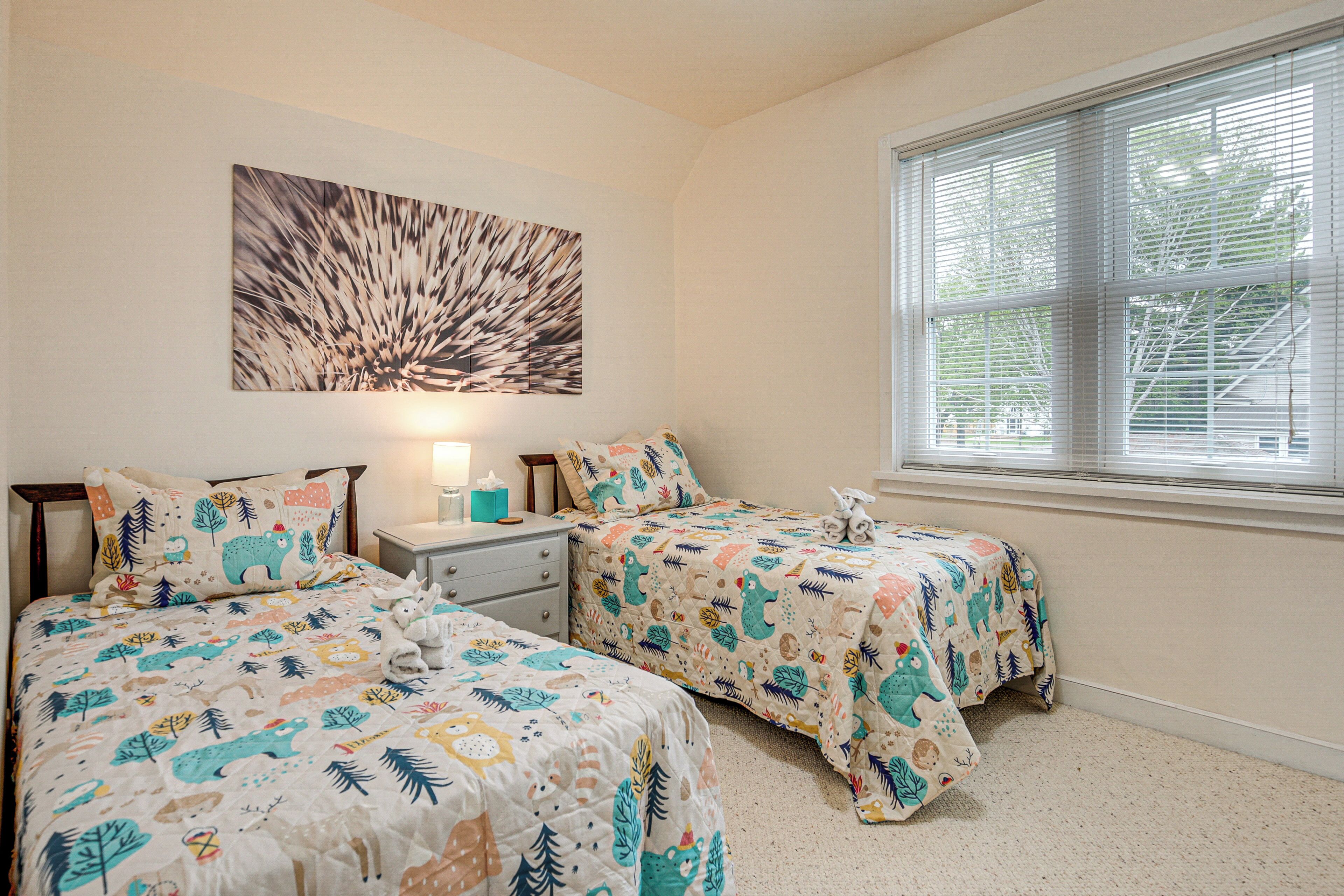 A bedroom with two beds, a nightstand, a lamp, and a window with blinds.