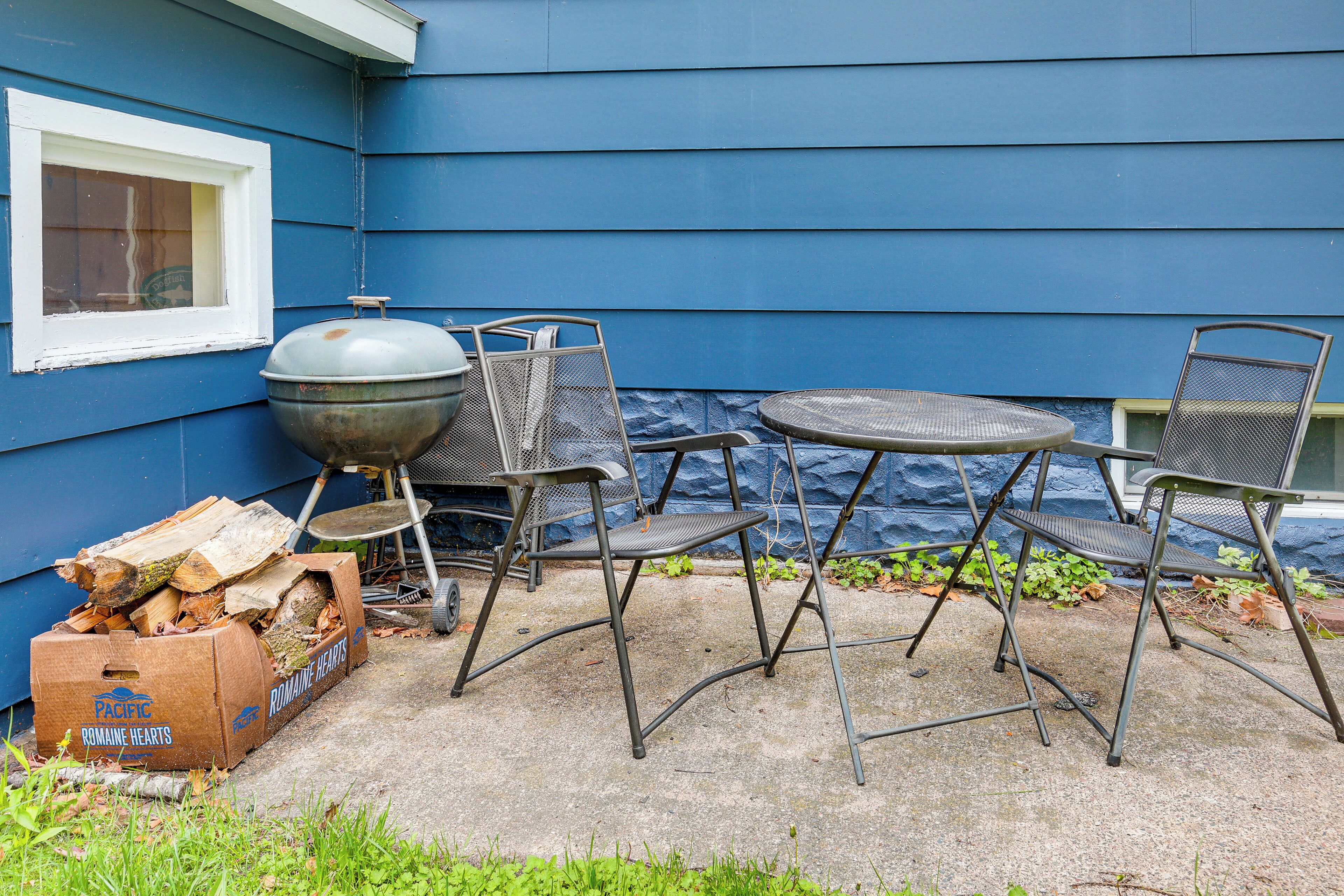 Une terrasse extérieure avec un barbecue, des chaises en métal et une table.