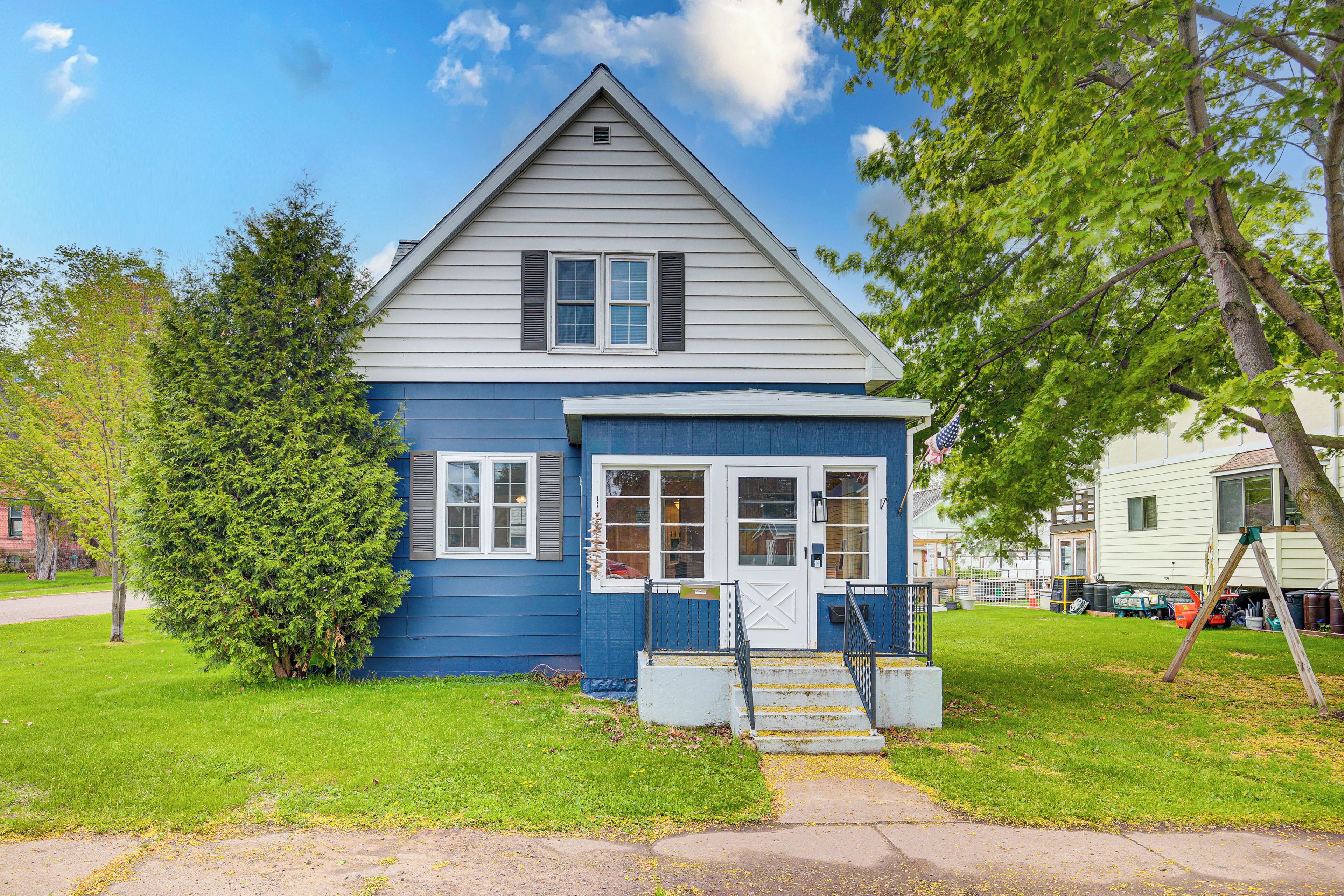 A two-story house with a front porch, a small front yard, and a tree.