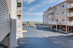 A beachfront apartment complex with multiple balconies, a parking area, and a view of the ocean. - Oceanfront Carolina Beach Condo w/ Pool & Views! (Carolina Beach)