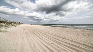 Uma extensa praia de areia com ondas suaves e céu nublado.