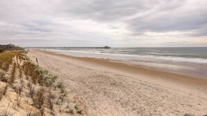 A beach with a long pier extending into the ocean, sandy dunes, and a cloudy sky. - Ocean Views + Resort Pool! N Topsail Beach Condo (Sneads Ferry)