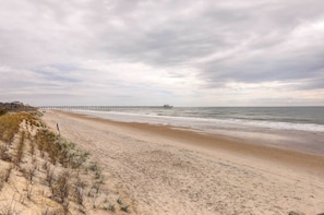 Ein Strand mit einem langen Steg, der ins Meer führt, Sanddünen und einem bewölkten Himmel.