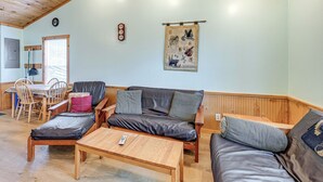 Een gezellige woonkamer met een houten plafond, een bank, een salontafel en een eethoek met stoelen en een tafel.