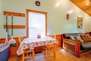 A dining area with a table set for two, wooden chairs, a window with blinds, and a wall-mounted clock. - Peaceful Bryson City Cabin - Fire Pit & Hot Tub! (Bryson City)