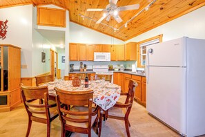 A wooden interior with a dining table set for four, a kitchen with wooden cabinets, a white refrigerator, and a ceiling fan. - Peaceful Bryson City Cabin - Fire Pit & Hot Tub! (Bryson City)