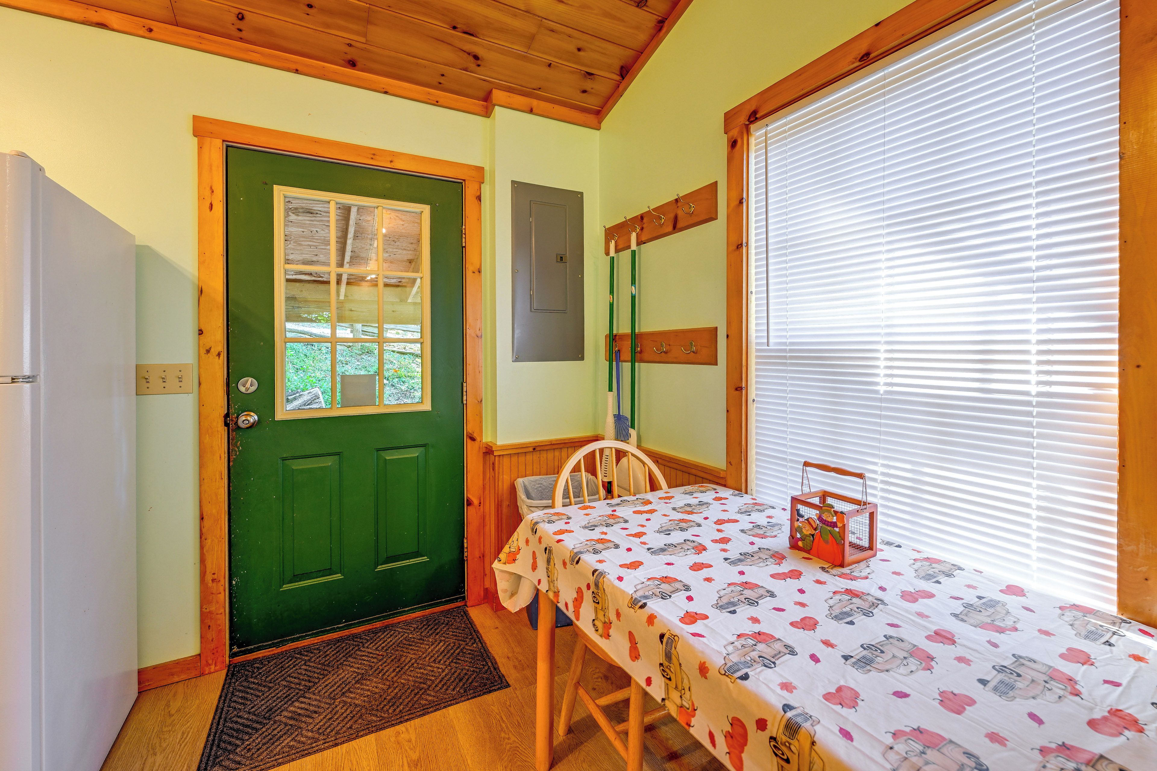 Una habitación con una puerta verde, una mesa con mantel estampado, una silla y una ventana con persianas.