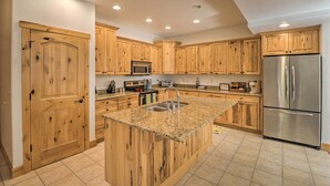 Una cocina con armarios de madera, encimeras de granito, refrigerador de acero inoxidable y un microondas.