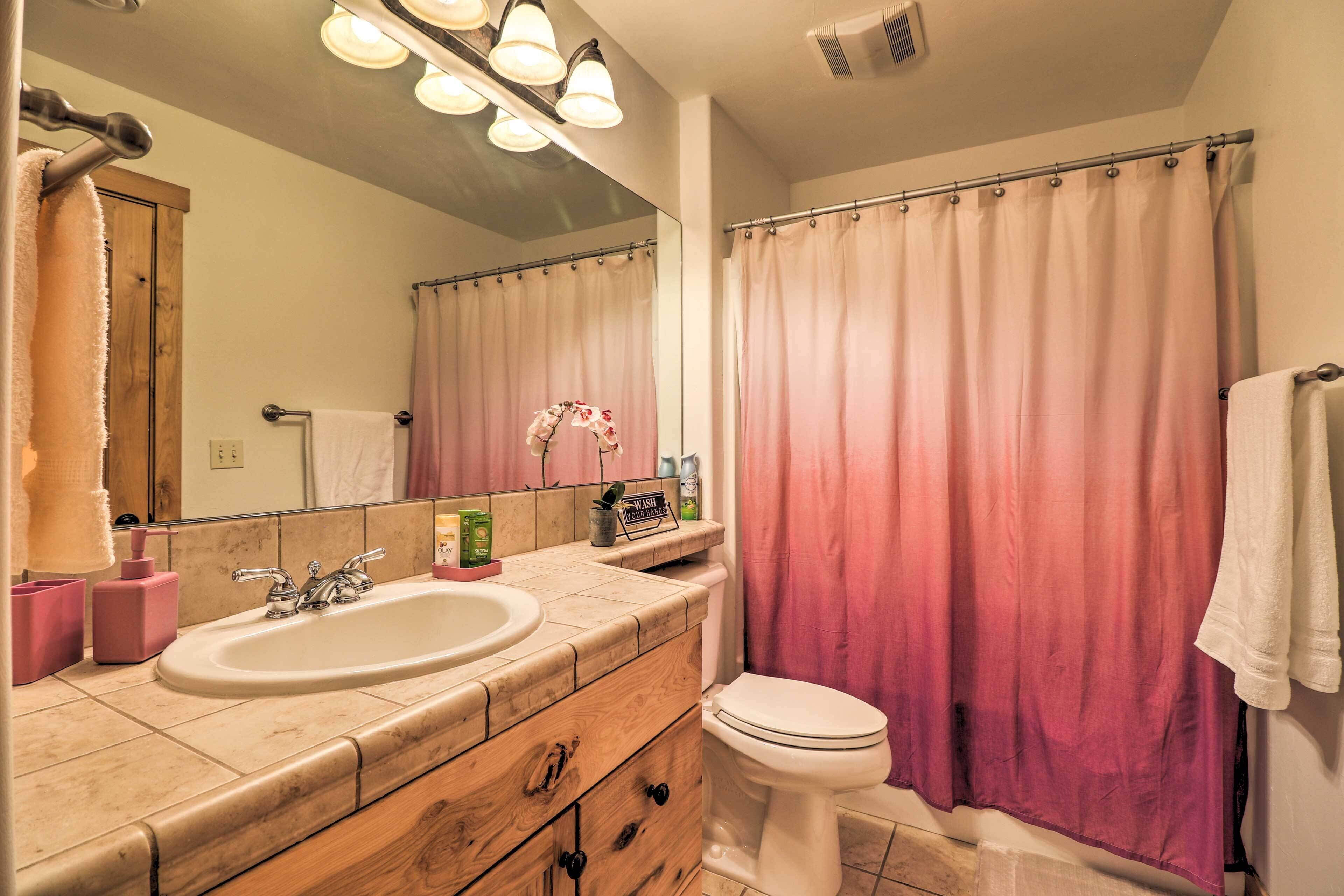 A bathroom with a wooden vanity, two sinks, a toilet, and a shower curtain.