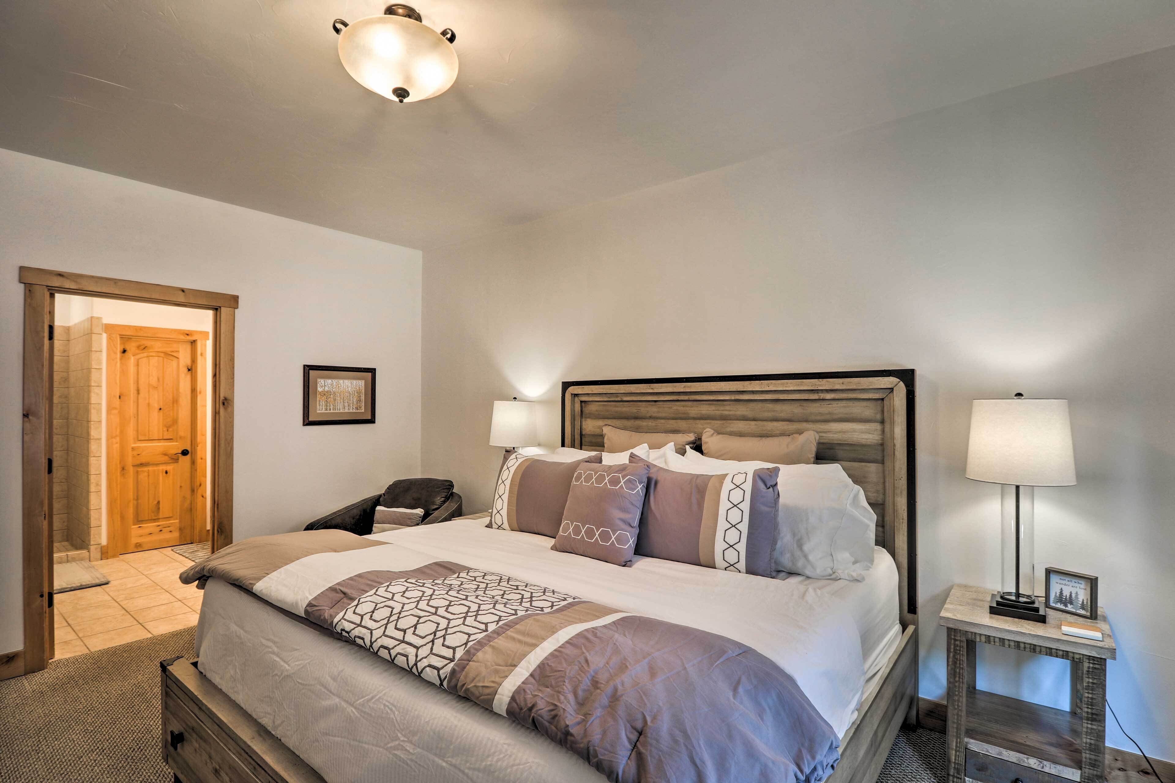 A bedroom with a large bed, two bedside lamps, a wooden headboard, and a door leading to another room.
