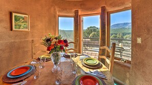 A dining table set with plates, glasses, and a vase of flowers, with a scenic view through large windows. - Peaceful New Mexico Retreat w/ Panoramic Mtn Views (Cleveland)