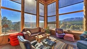 A spacious room with large windows offering a mountain view, a cozy seating area with a sofa and chairs, and a small wooden table. - Peaceful New Mexico Retreat w/ Panoramic Mtn Views (Cleveland)