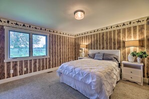 A bedroom with a large bed, two bedside tables, a nightstand, a window, and a wall with a wooden panel design.