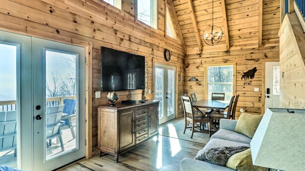 A log cabin interior with a wooden dining area, a sofa, a television, and a fireplace. - Peaceful Free Union Cabin w/ Deck & Mtn Views (Dyke)