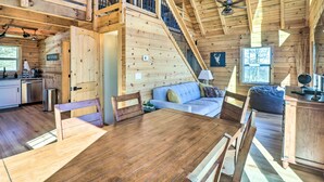 A wooden cabin interior with a dining table, chairs, a sofa, a staircase, and a kitchen area. - Peaceful Free Union Cabin w/ Deck & Mtn Views (Dyke)