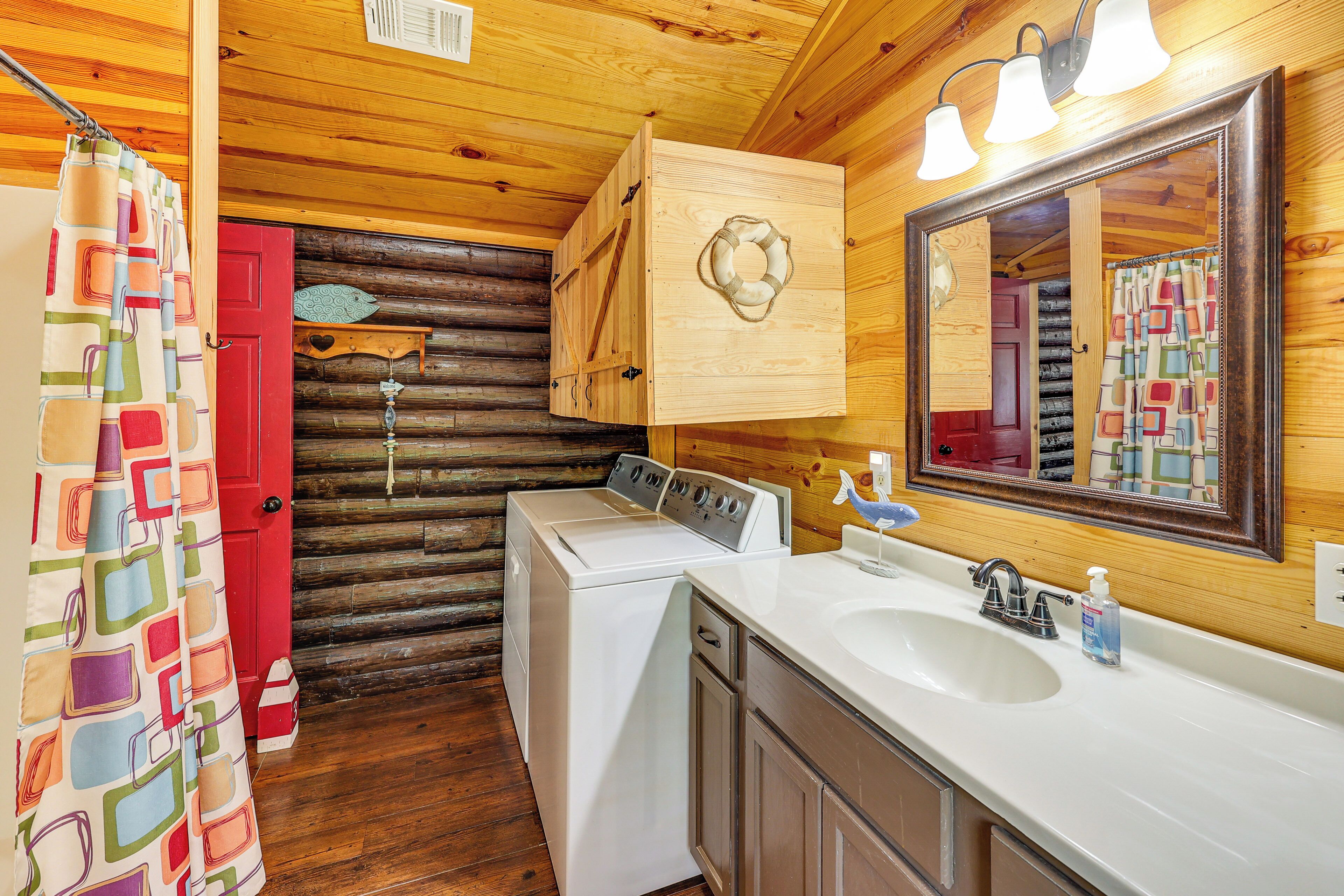 A wooden cabin bathroom with a wooden door, a washing machine, a sink with a mirror, and a shower curtain.