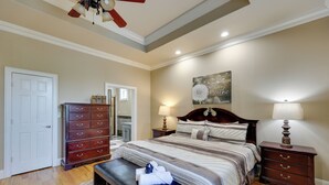 A bedroom with a large bed, wooden dresser, and a bench with towels. - Game Room & Private Pool: Home in Hot Springs! (Hot Springs)