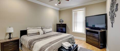 A bedroom with a bed, nightstand, TV, and a ceiling fan.