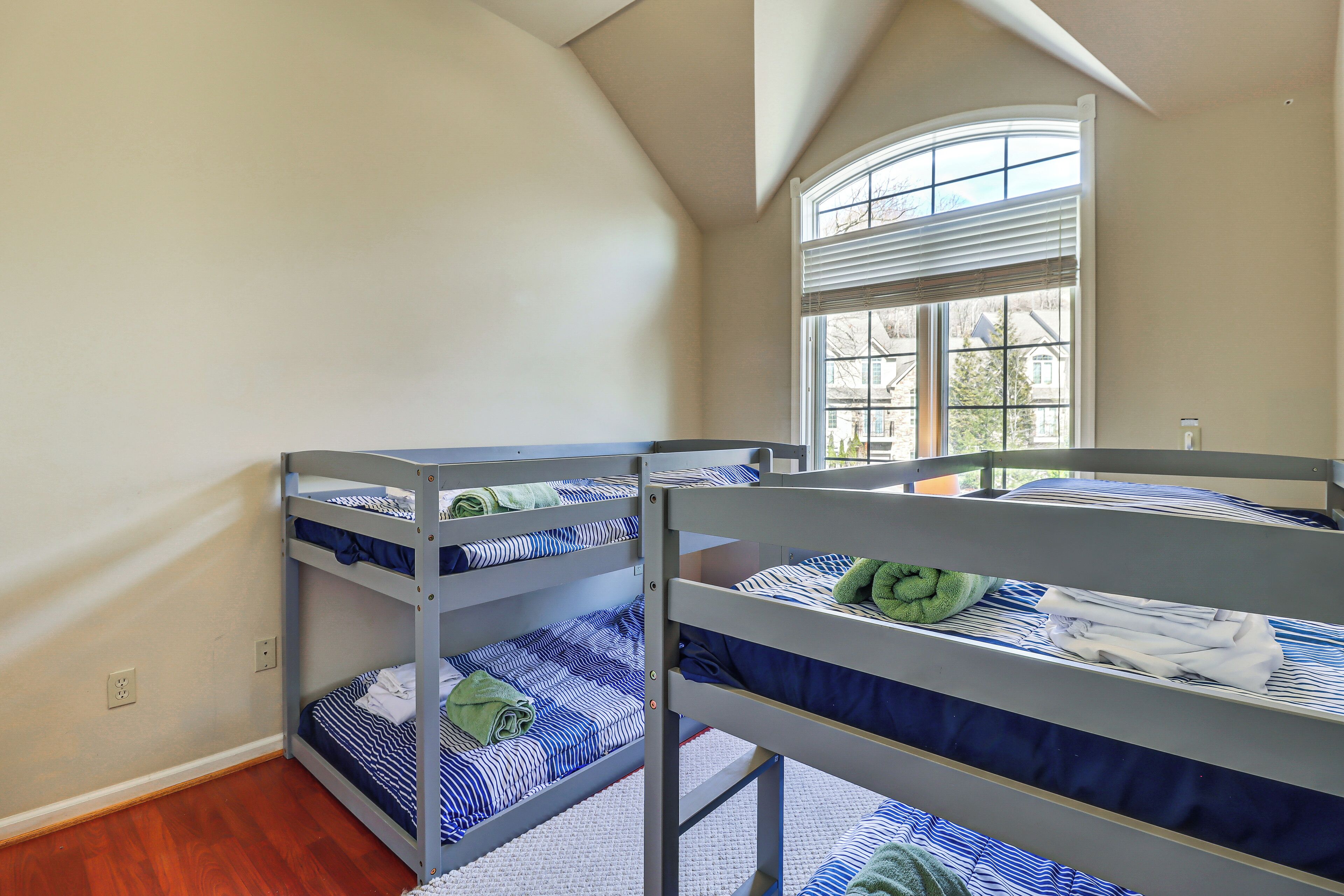 A dormitory room with bunk beds, a large window with blinds, and a wooden floor.