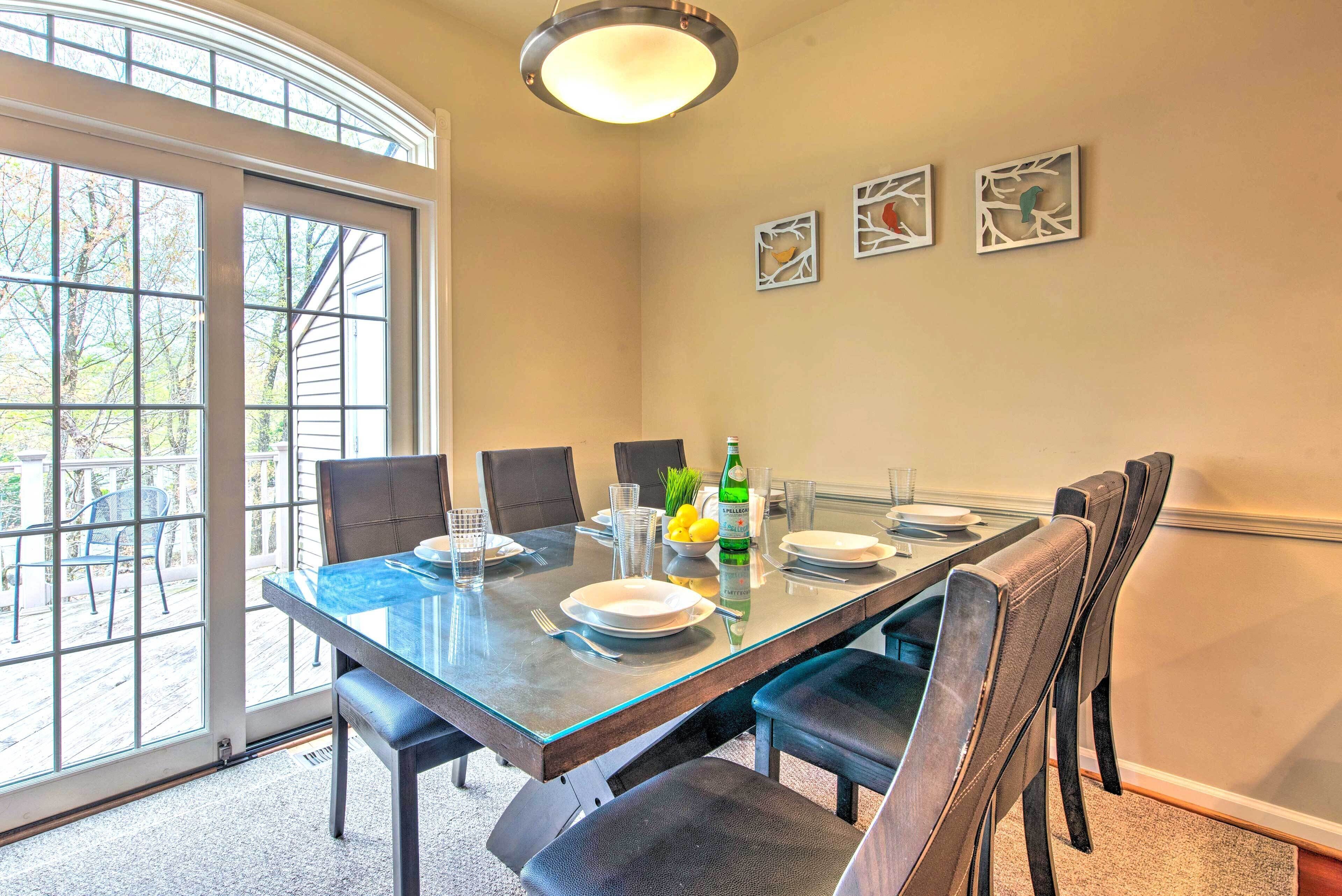 A dining area with a glass table, chairs, and a view through a large window.