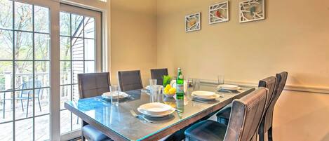 A dining area with a glass table, chairs, and a view through a large window.