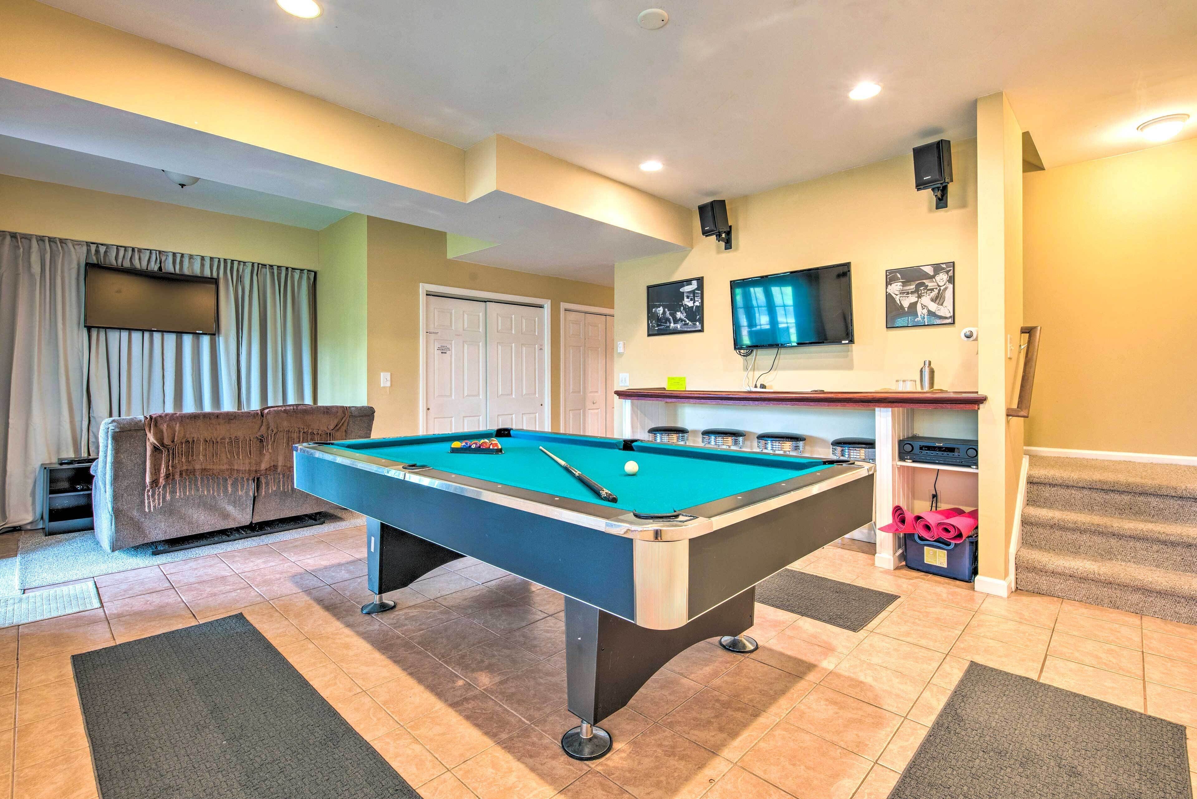 A pool table in a room with a sofa, a television, and a staircase.