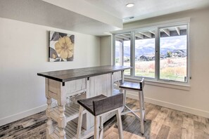 A kitchen with a wooden island, two bar stools, a large window with a view of a mountain and houses, and a floral artwork on the wall. - Scenic Eden Gem w/ Hot Tub ~ 6 Mi to Ski Area (Eden)