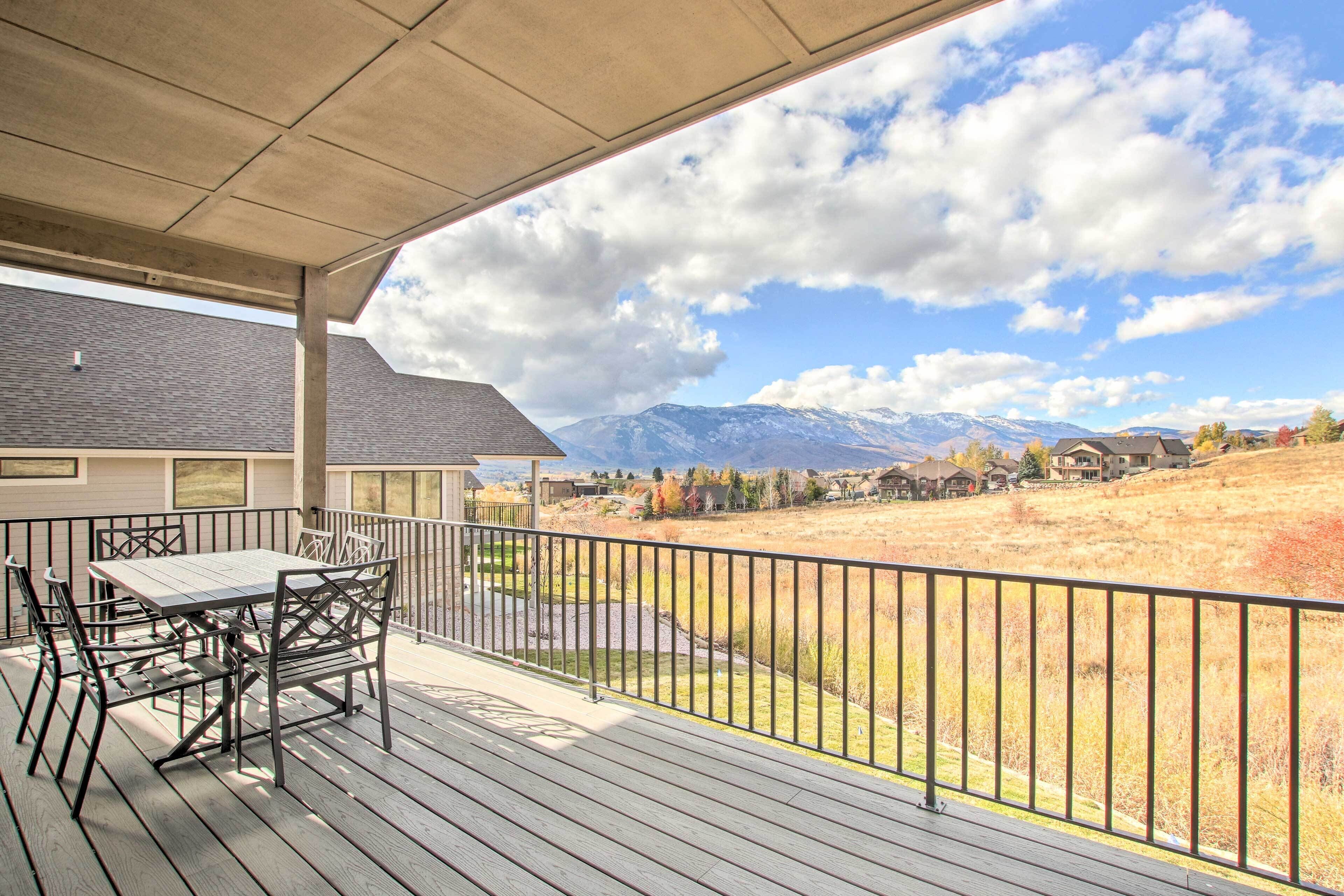 A covered outdoor area with a table and chairs, overlooking a mountainous landscape.