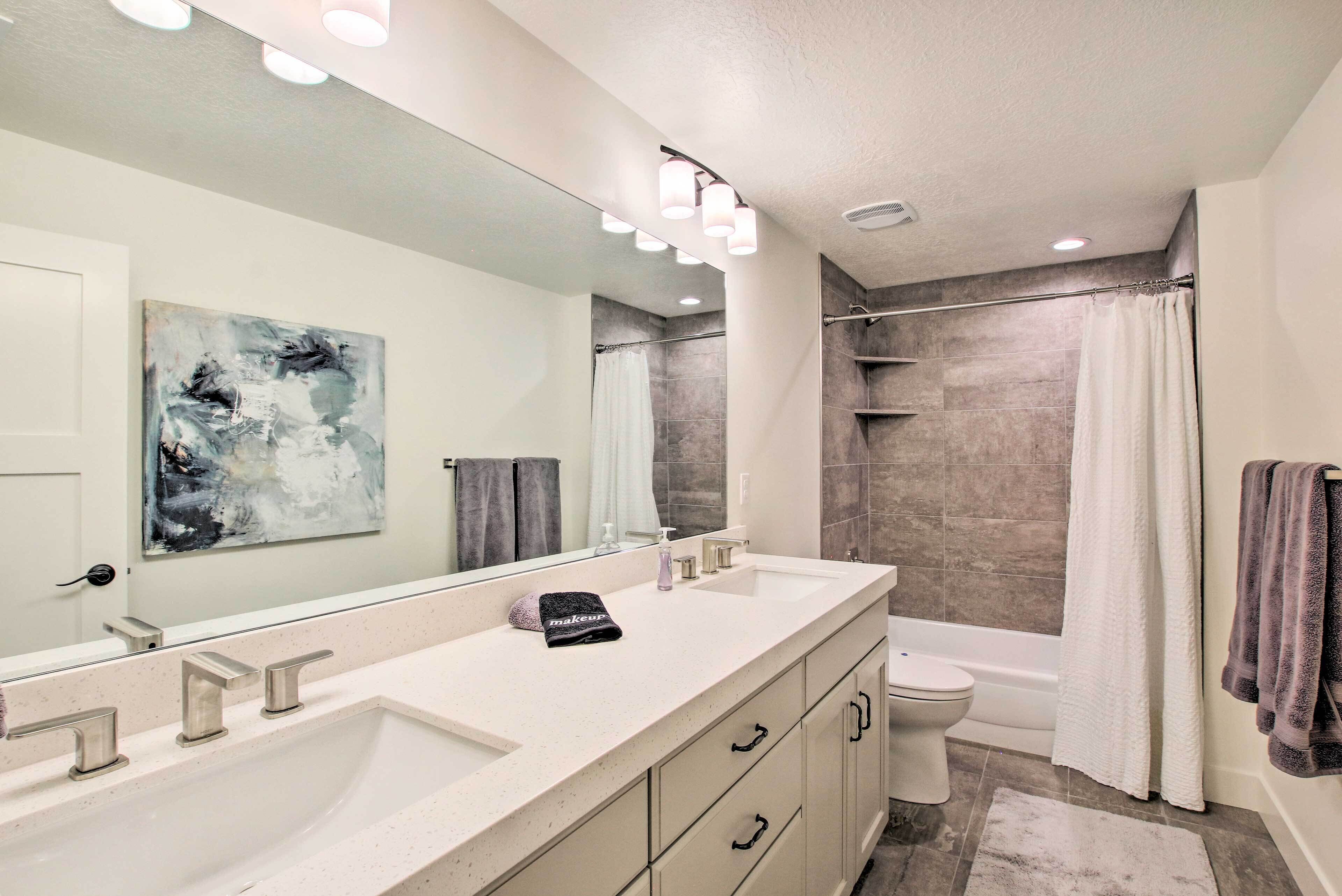 A modern bathroom with a large mirror, two sinks, a toilet, and a shower area.