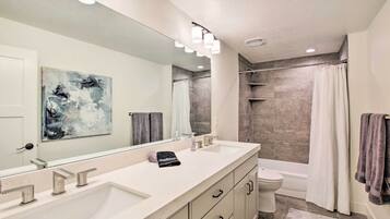 A modern bathroom with a large mirror, two sinks, a toilet, and a shower area.