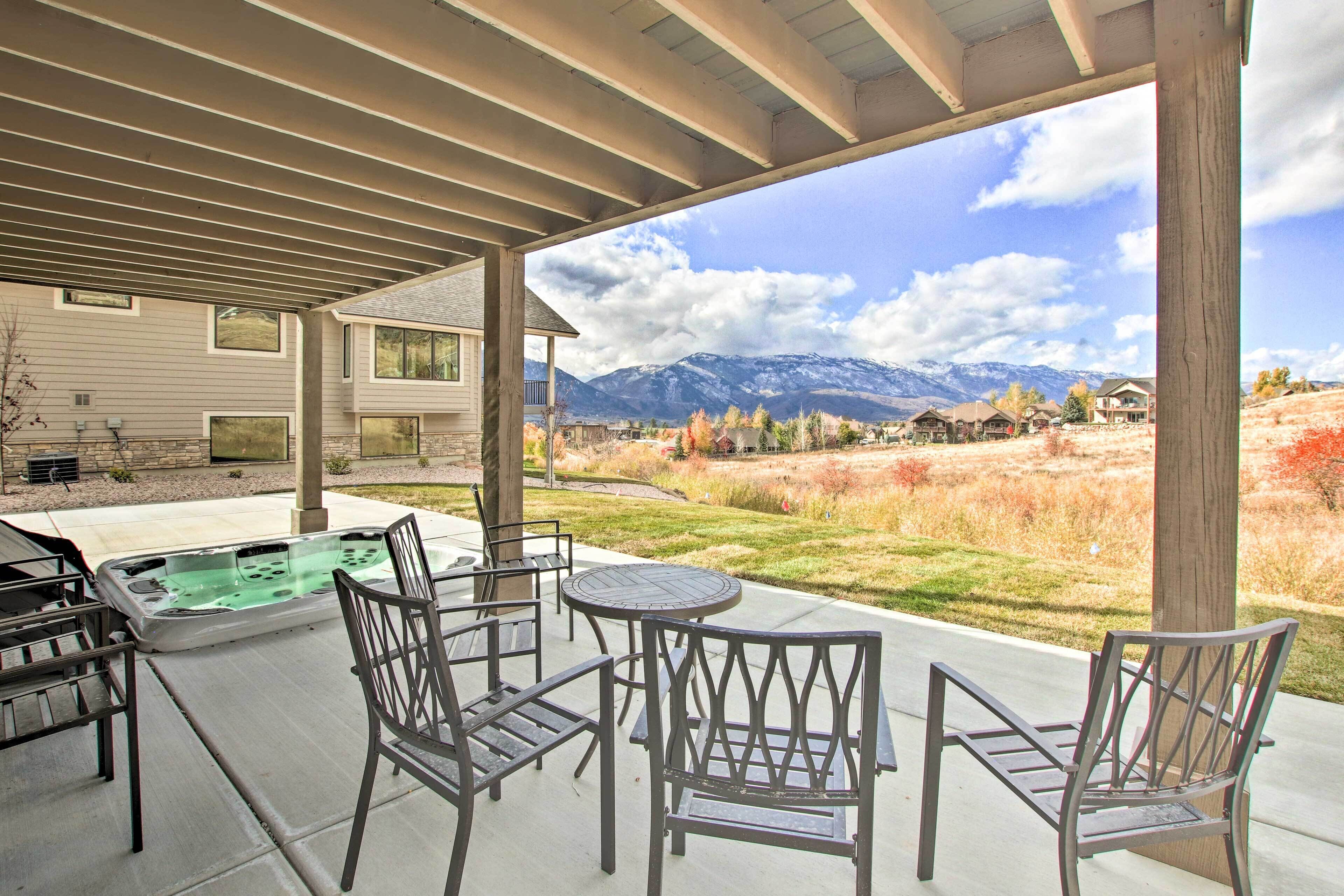 A covered patio with a hot tub, chairs, and a view of mountains.