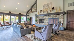 A spacious living room with a stone fireplace, comfortable seating, and large windows offering a view of the outdoors.