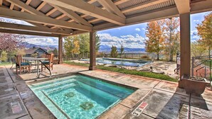 A covered outdoor pool area with a hot tub, patio furniture, and a view of mountains and trees.