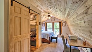 Un dormitorio acogedor en el ático con techo de madera, cama, escritorio y un amplio ventanal.
