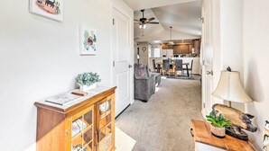 A hallway with a wooden cabinet, a small table with a plant, and a lamp. There is a ceiling fan and a door leading to a kitchen area. - Prismatic Boise Retreat w/ Fenced Backyard! (Boise)