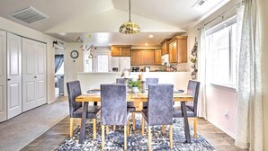 A dining area with a wooden table and chairs, a hanging light fixture, and a view of the kitchen in the background. - Prismatic Boise Retreat w/ Fenced Backyard! (Boise)