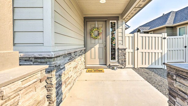 A house entrance with a gray door, a welcome mat, a stone wall, and a gated driveway. - Prismatic Boise Retreat w/ Fenced Backyard! (Boise)
