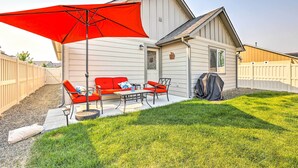 A house with a patio area featuring a red umbrella, a sofa, and a table. - Prismatic Boise Retreat w/ Fenced Backyard! (Boise)