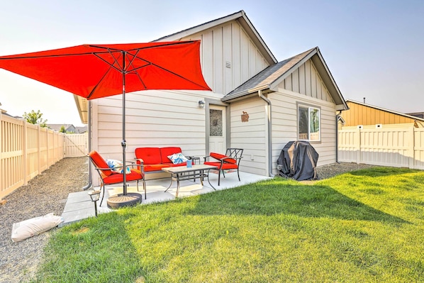 Uma casa com área de varanda, incluindo um guarda-sol vermelho, um sofá, uma mesa e uma cadeira.