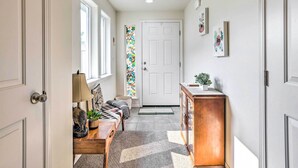 A hallway with a bench, a door, a stained glass window, and a small plant on a cabinet. - Prismatic Boise Retreat w/ Fenced Backyard! (Boise)