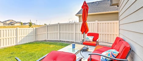 A patio with red chairs and a table, a red umbrella, and a white fence.