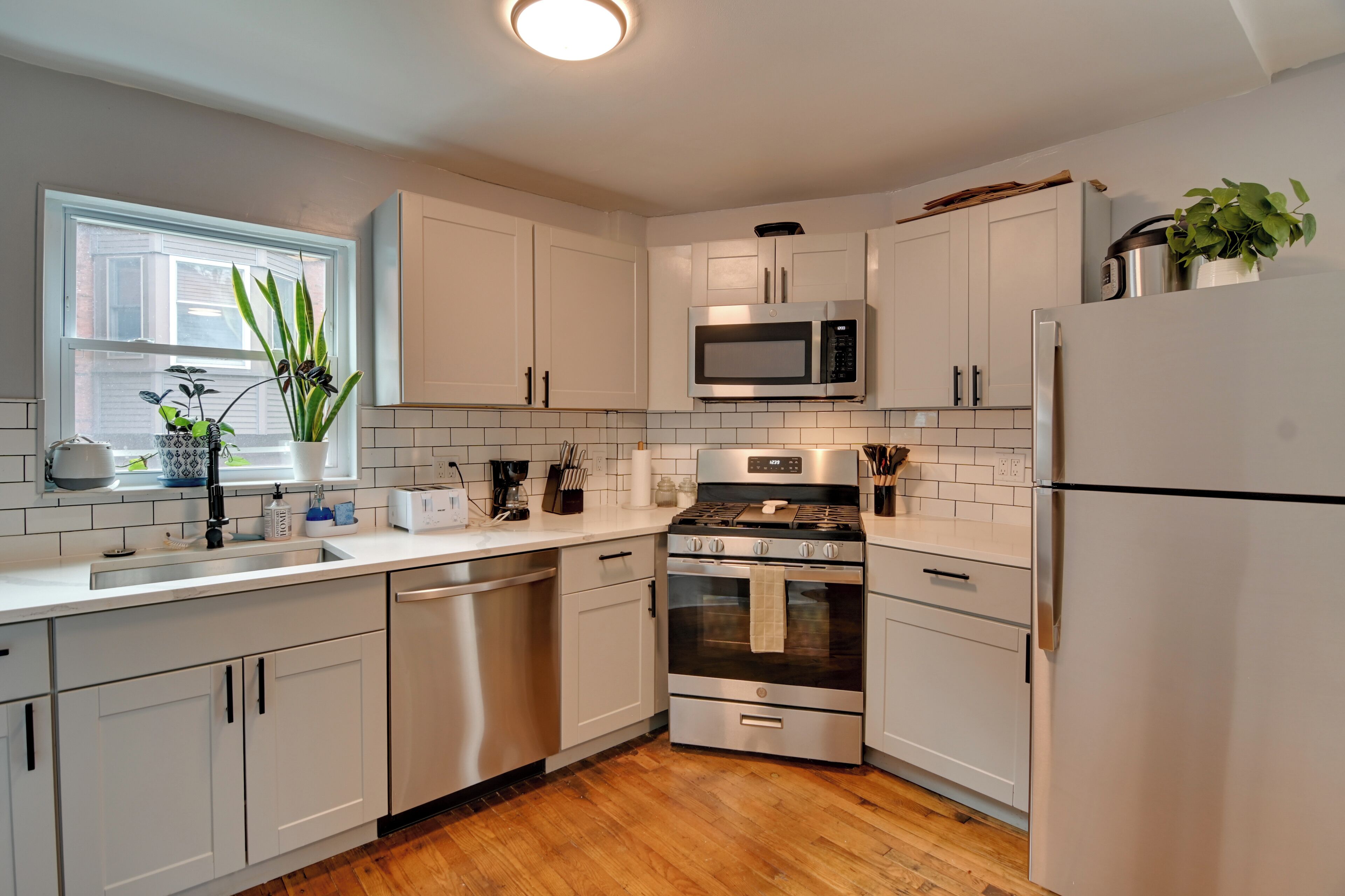 A modern kitchen with white cabinets, stainless steel appliances, and a wooden floor.