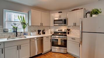 A modern kitchen with white cabinets, stainless steel appliances, and a wooden floor.