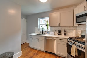 A modern kitchen with white cabinets, a stainless steel dishwasher, a gas stove, and a window with a plant. - Pittsburgh Home Near Frick Park, 7 Mi to Dtwn (Pittsburgh)
